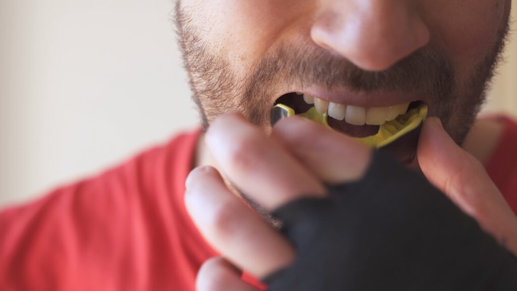 Young male putting mouthguard before boxing sparring training