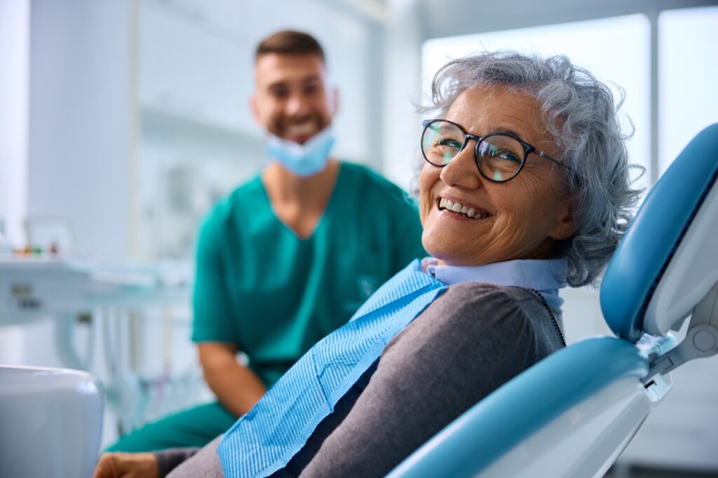 Happy senior woman at dental clinic looking at camera. Her dentist is in the background.